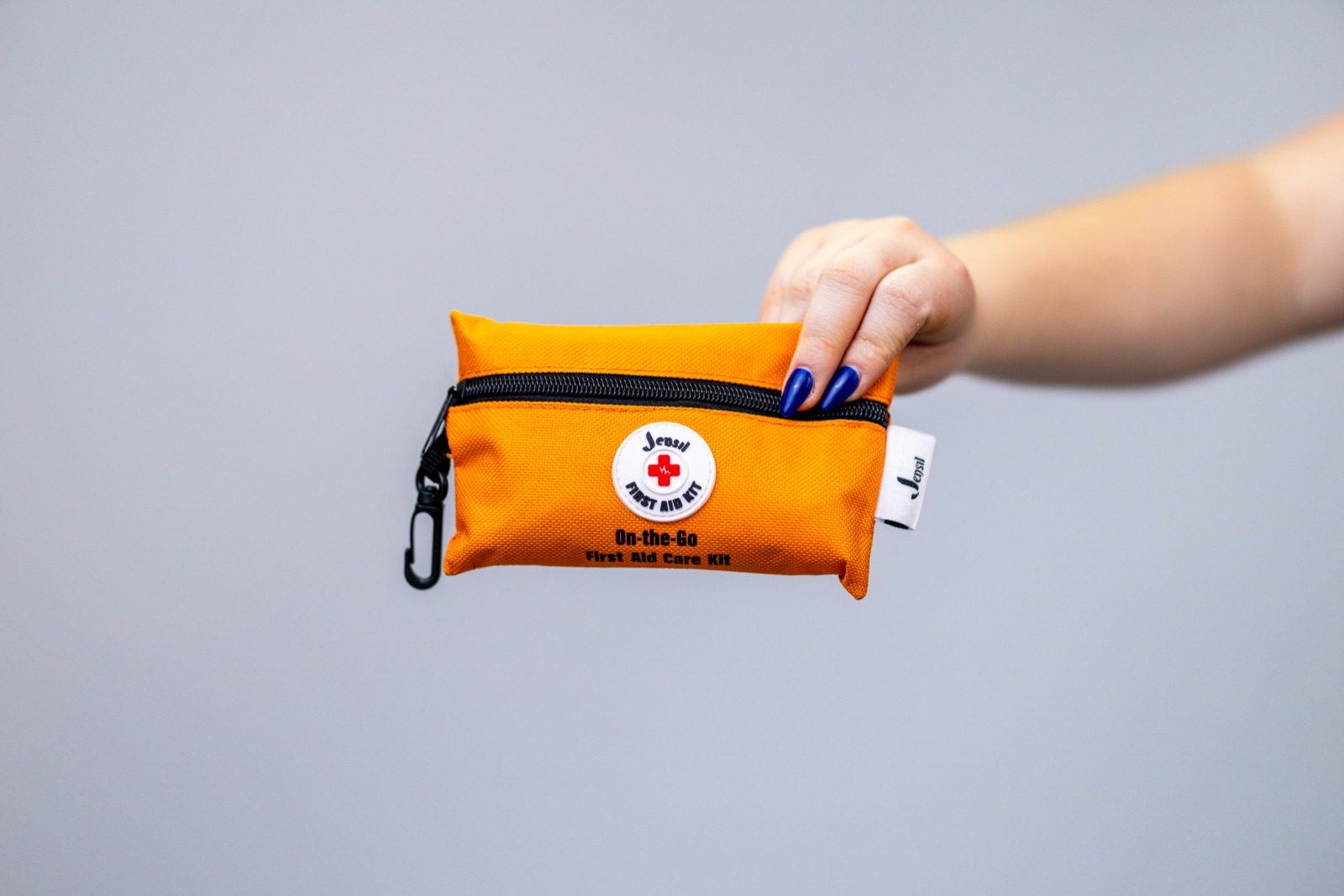 A hand holding the orange Jensil Travel Ready Kit